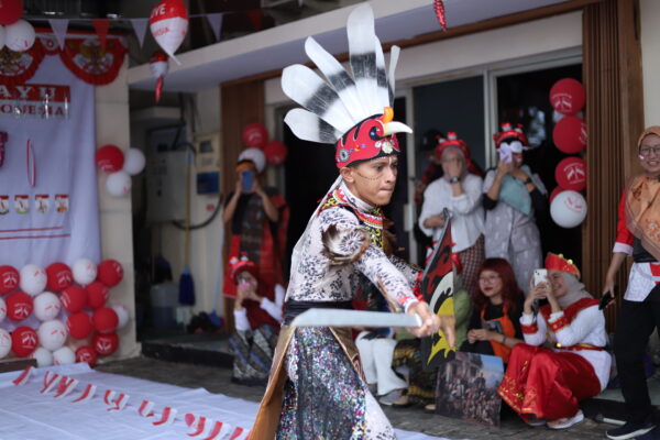 A person dressed in traditional Dayak attire performs with a sword and shield during a cultural fashion show at Bahtera Adi Jaya Tekno