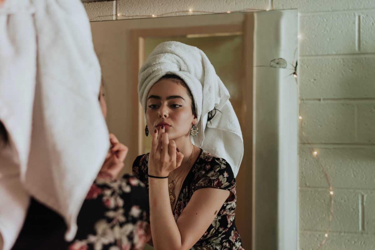 woman applying skincare with vintage ingredients in front of mirror