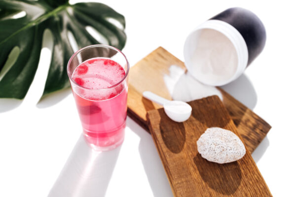 White glutathione powder in a glass container, beside a glass of pink-colored water.