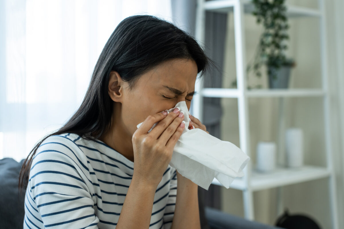 Woman sneezing into a tissue, seeking relief from allergy symptoms at home.